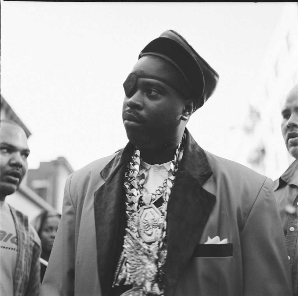 A man, rapper Slick Rick, photographed in a suit, with heavy jewelry, and an eye patch.