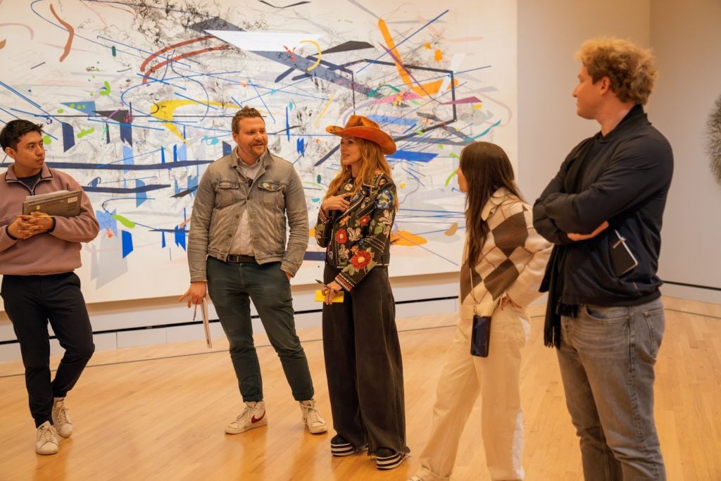 a crowd of people stand in museum, a large abstract canvas is on the wall behind them
