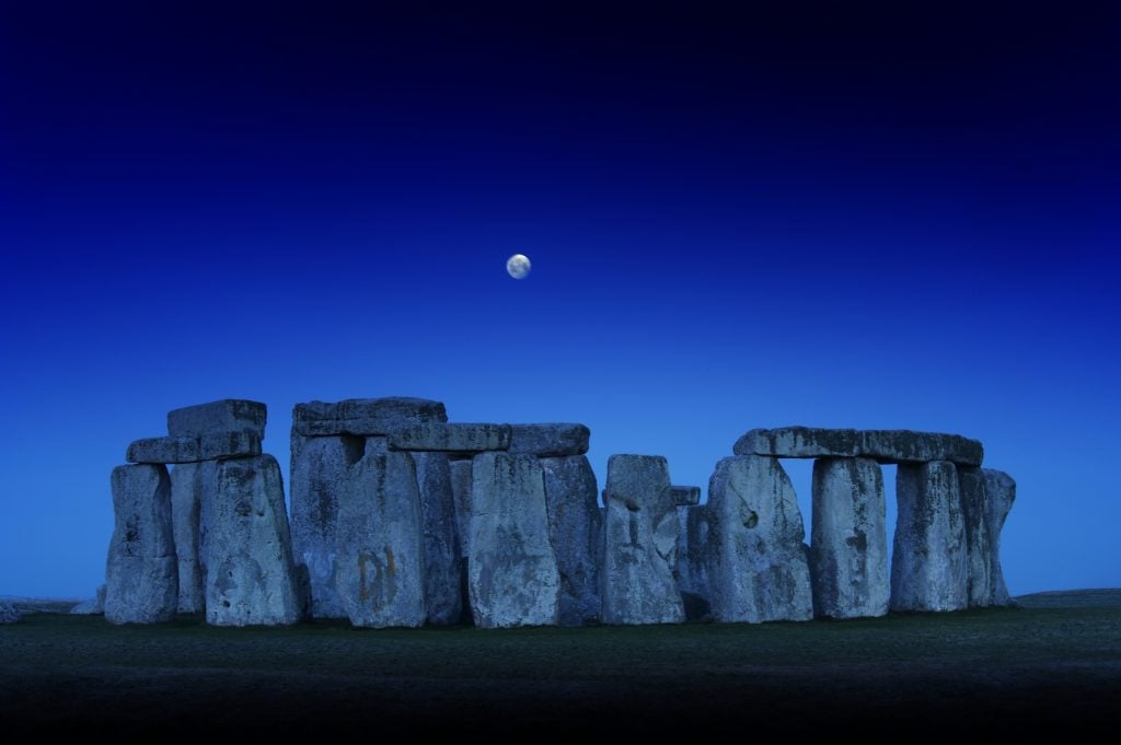 the moon above Stonehenge in a night blue sky