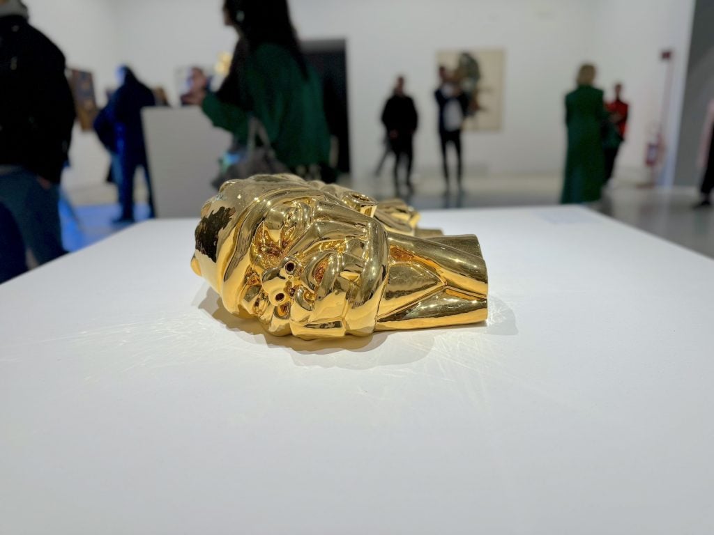 A sculpture of a shining gold head set on its side on a pedestal