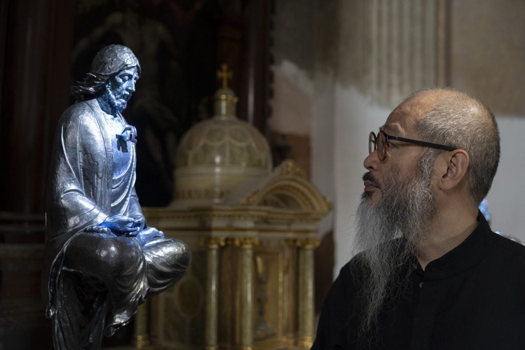 A man with long beard looking at a sculpture