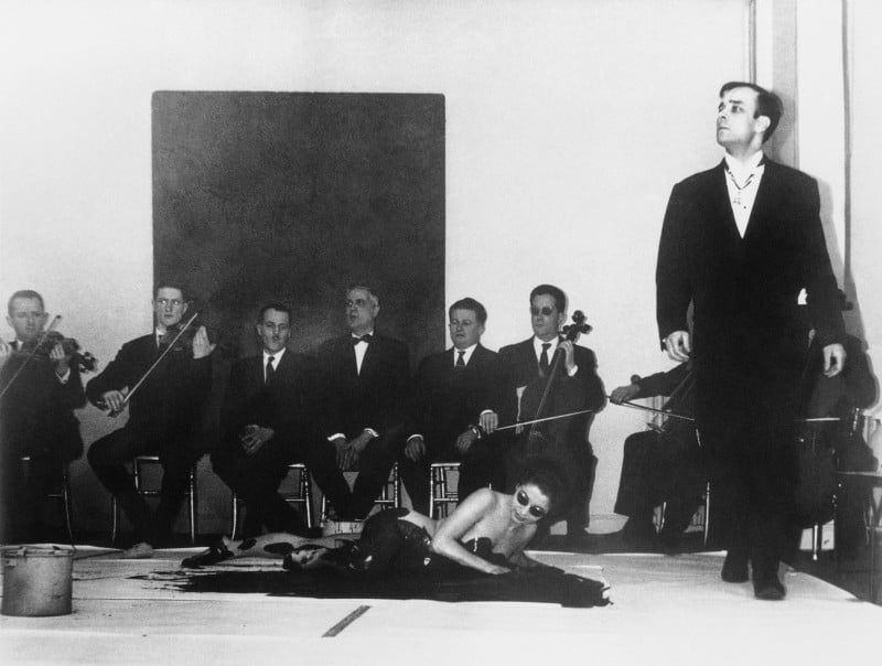 a woman writhes in paint atop a canvas as an orchestra plays and Yves Klein conducts 