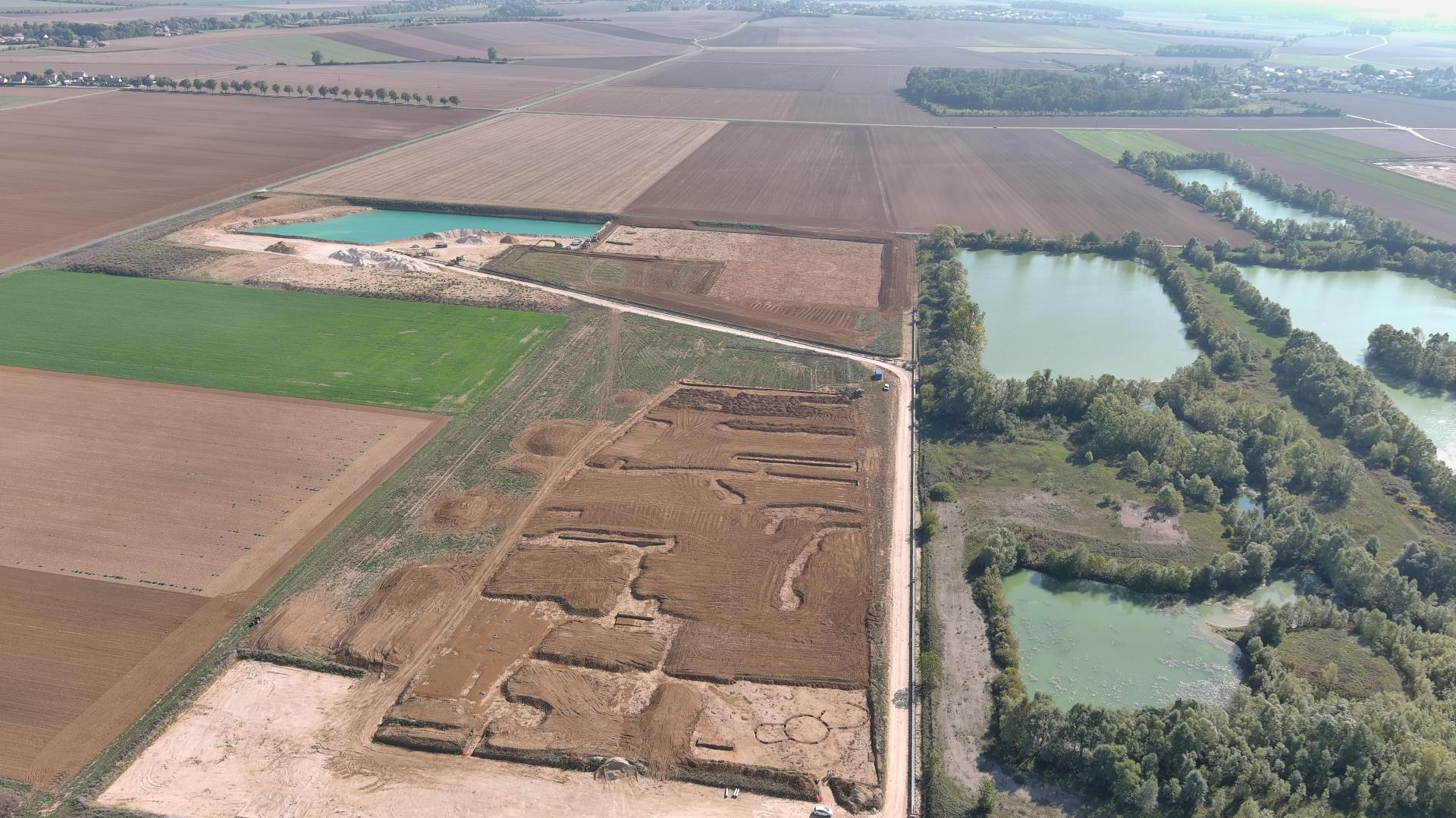 An aerial photograph of a varied landscape including green fields and dirt fields on the left with several ponds on the right