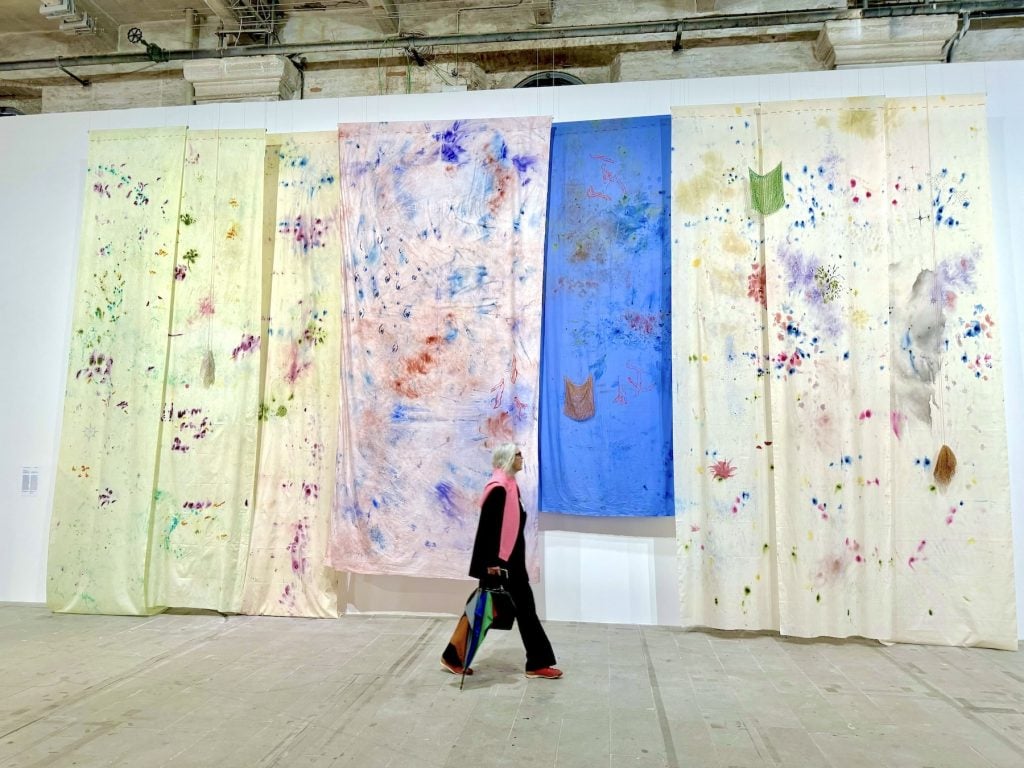 A woman walks back an artwork made of large hanging textile panels