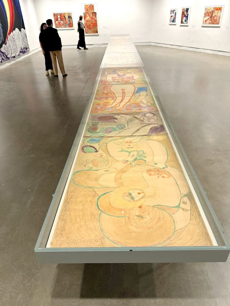 A long watercolor pencil drawing featuring images of women in a tabletop case in an art gallery