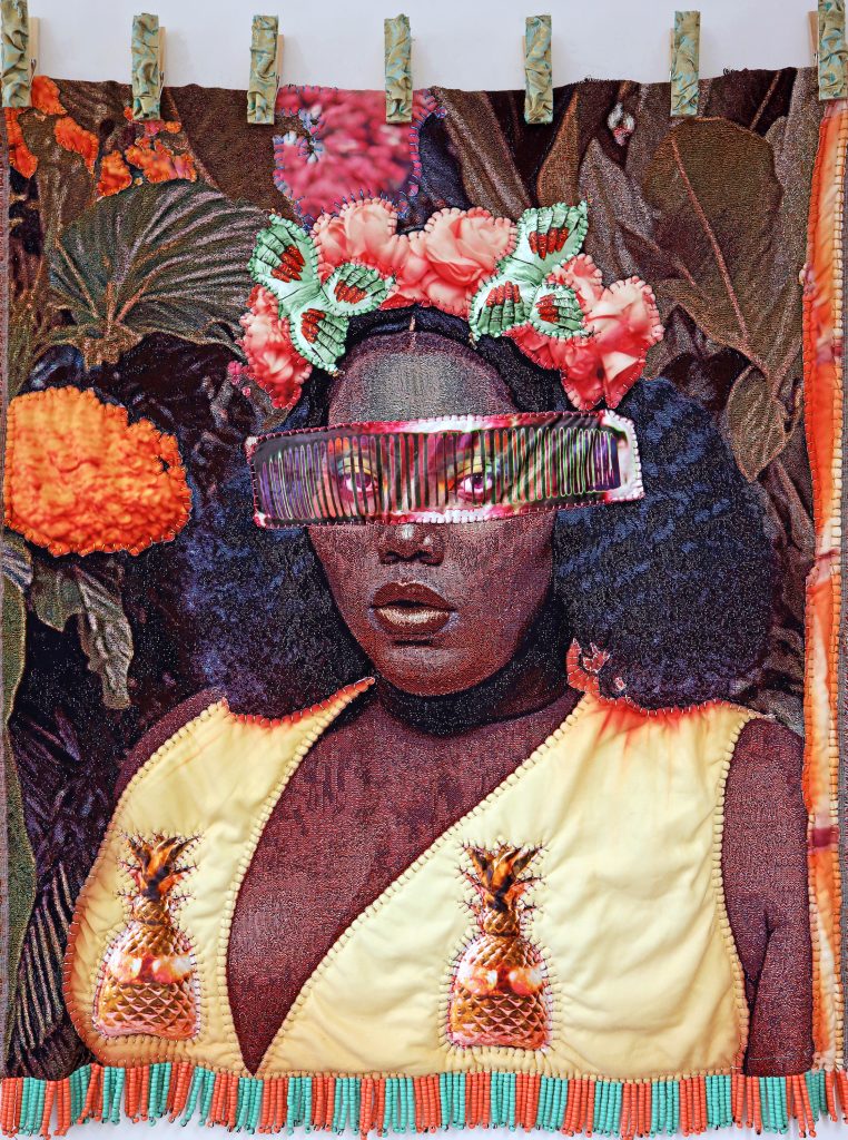 A textile and bead depiction of black woman looking out at the viewer with a fringed eye apparatus. The bottom length has fringed beads, and is held atop by clips.
