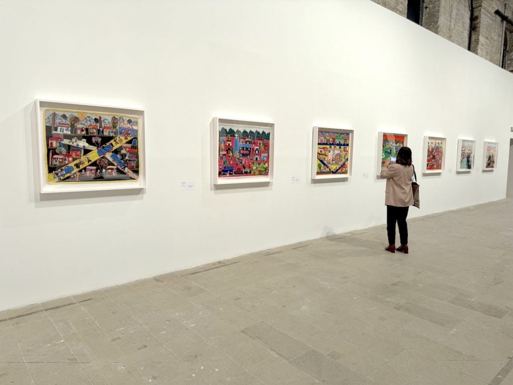 A woman takes a photo of various artworks made from colorful stretched burlap sacks displayed in an art gallery