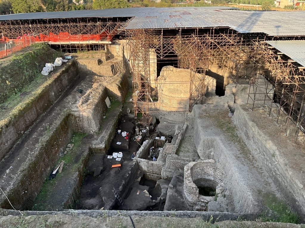 A large excavation site with a kiln and two other stone structures, partially surrounded by scaffolding