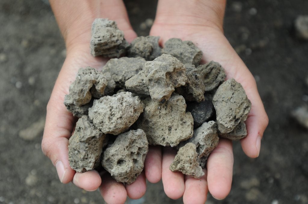 A pair of hands holding a pile of volcanic rock.