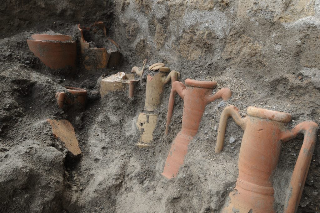 A series of ancient amphora vessels seen partially excavated from a wall of soil