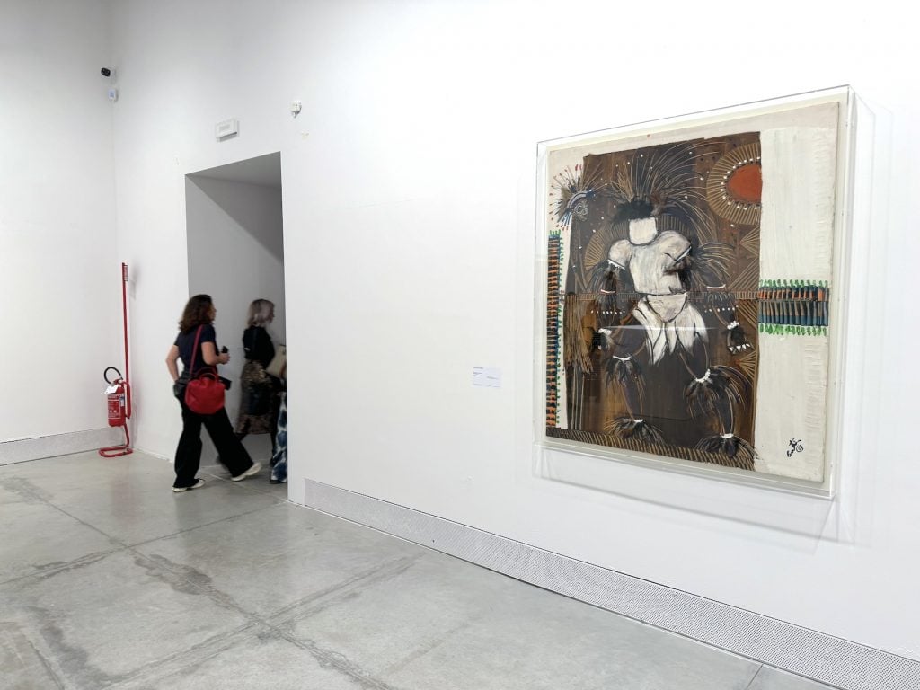 A woman enters a passage next to a large painting of a faceless figure