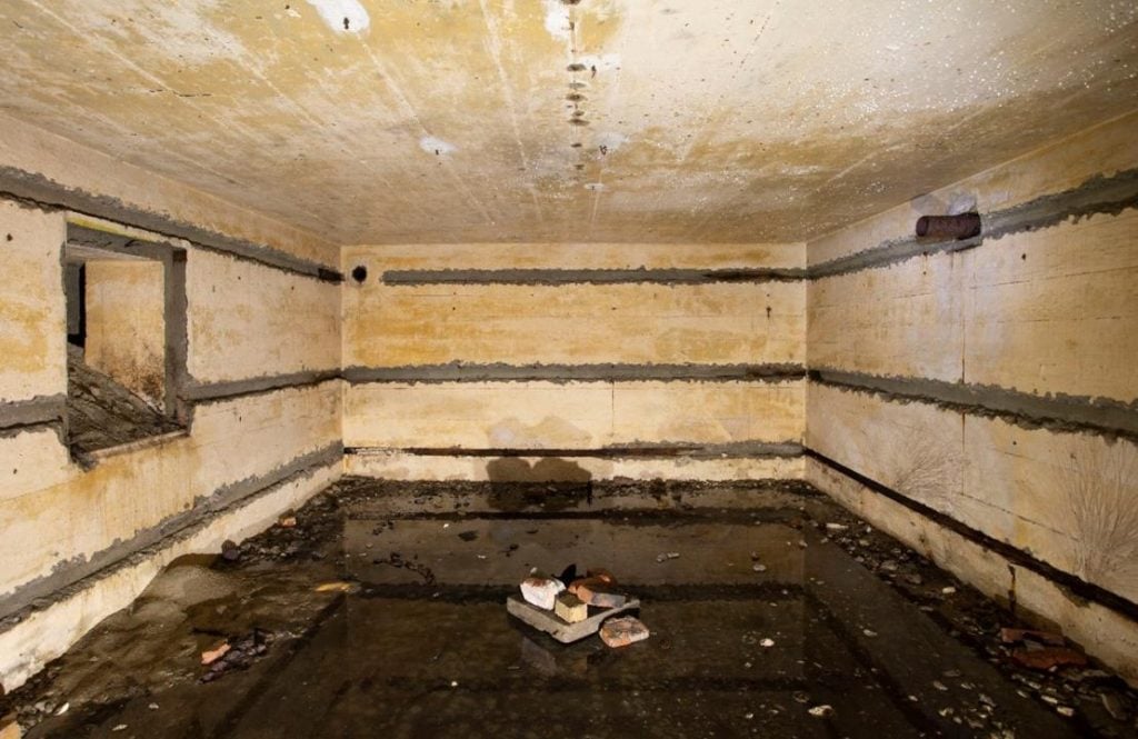 A photograph of the sparse white-walled inside of an 80 year old bunker, with dark barrren floors and three horizontal black lines marking its walls