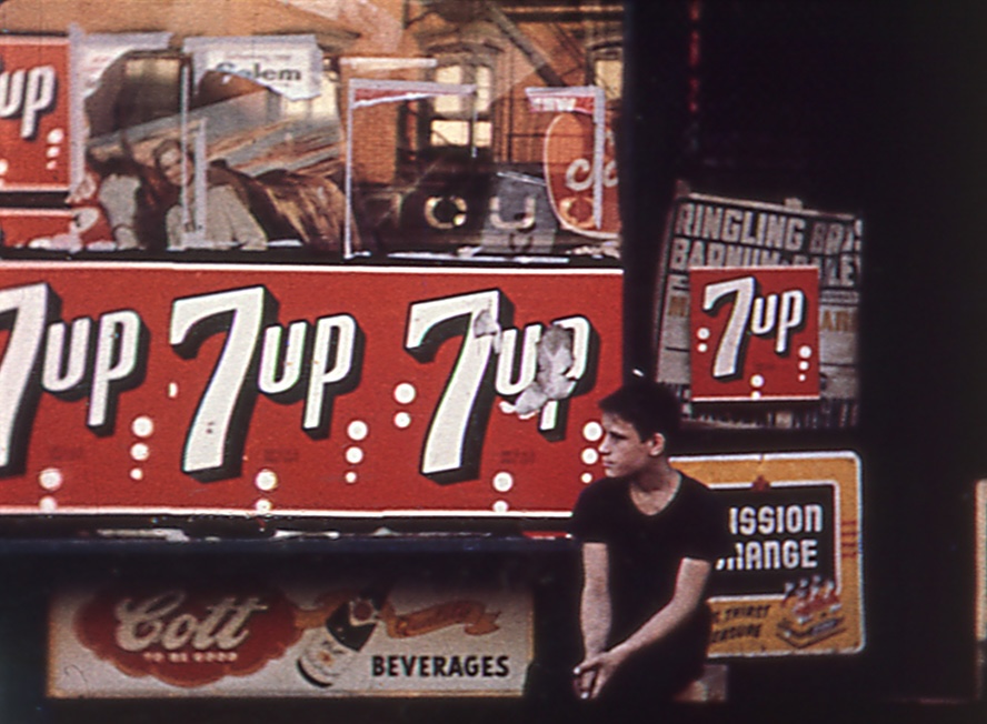 A young man sits in front of posters advertising 7 Up soda