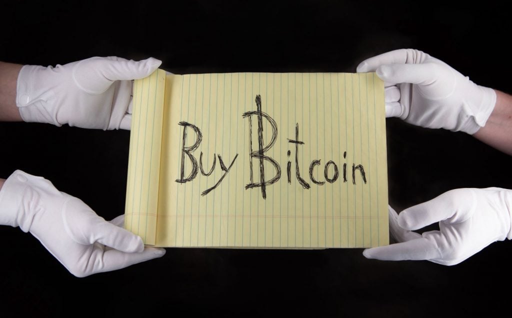four white gloved hands holding a yellow sign with the words 'Buy Bitcoin'