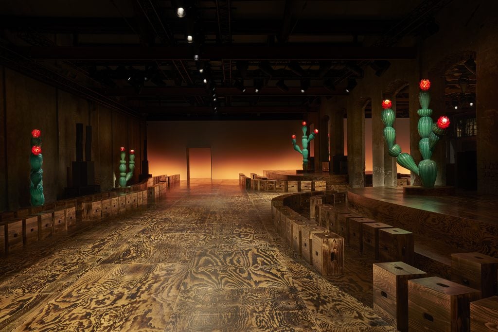 a wooden fashion show set has minimalist boxes for seating and sculptural cacti 