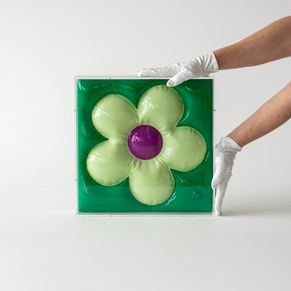 A photograph of a green resin sculpture made to look like a plastic inflatable, handled by an off-screen professional whose white gloves are holding the piece