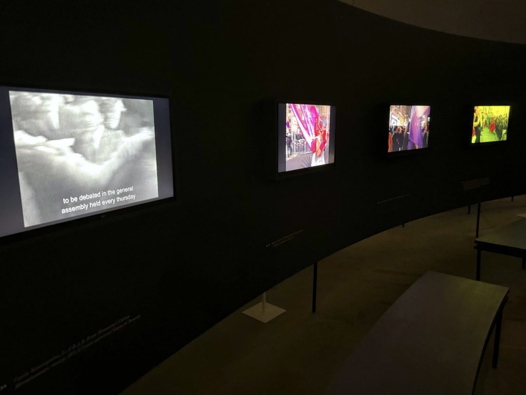 Four small video play mounted on a curving wall in a darkened gallery