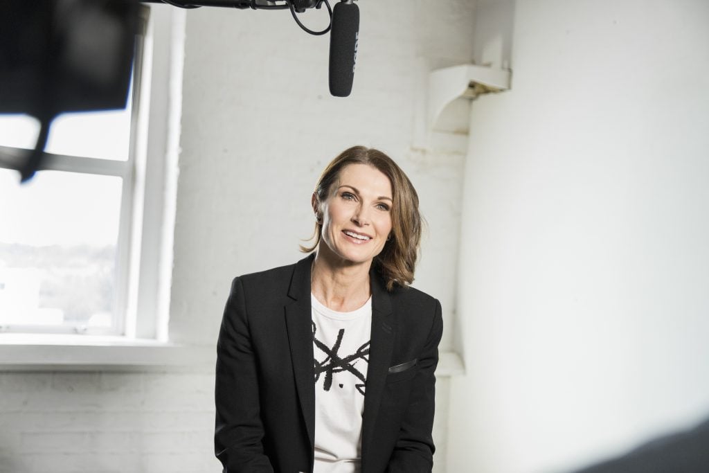 Dr Clare McAndrew sitting beneath a overhead microphone in a black blazer and graphic tee.