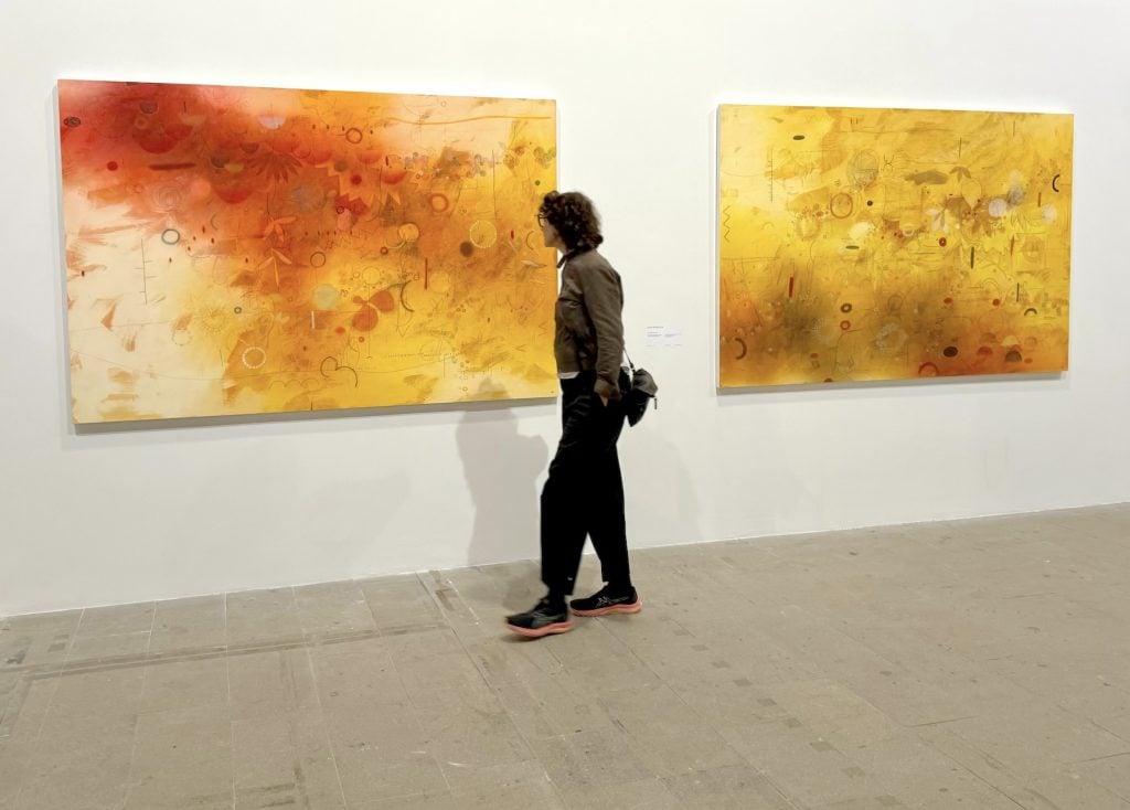 A figure observes two orange and yellow toned abstract paintings