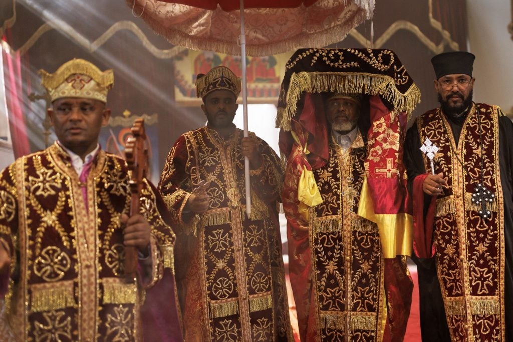 Men in ceremonial outfits laced with gold patterning, while one holds aloft a sacred tabot warpped in ceremonial cloths.