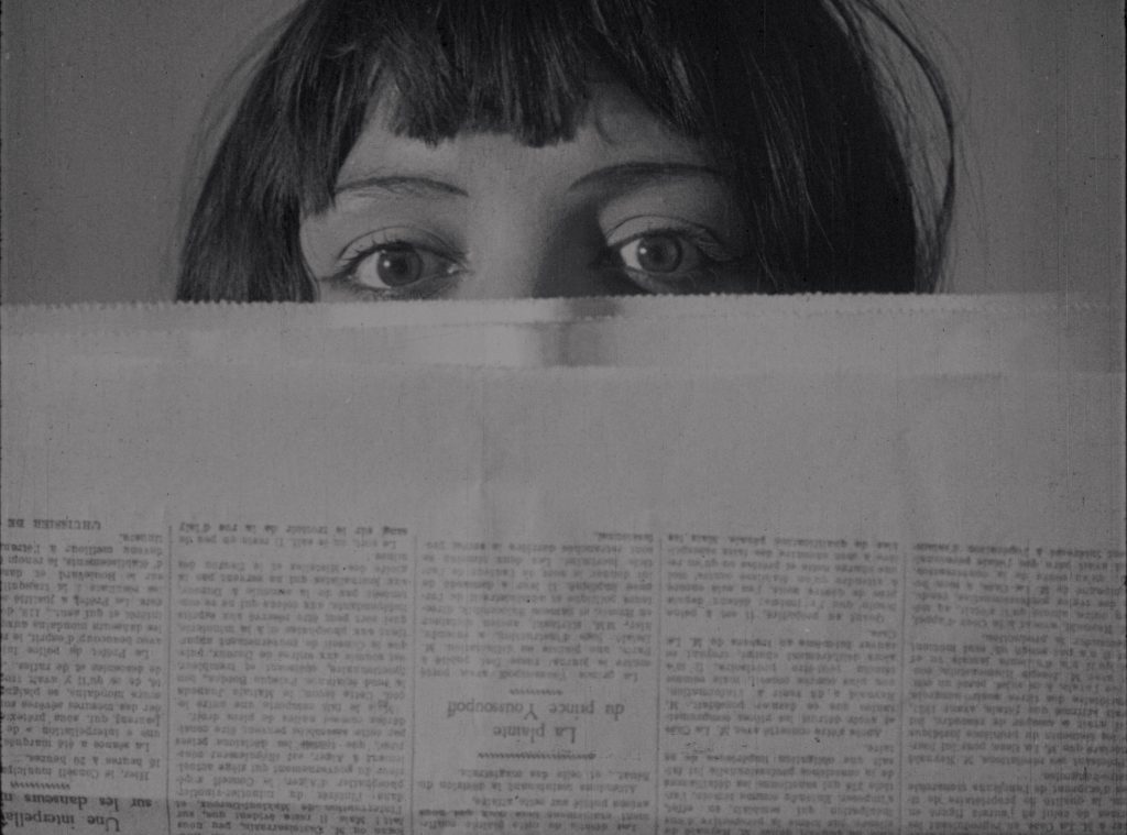 A woman's eyes appear above a newspaper she holds in front of her face.