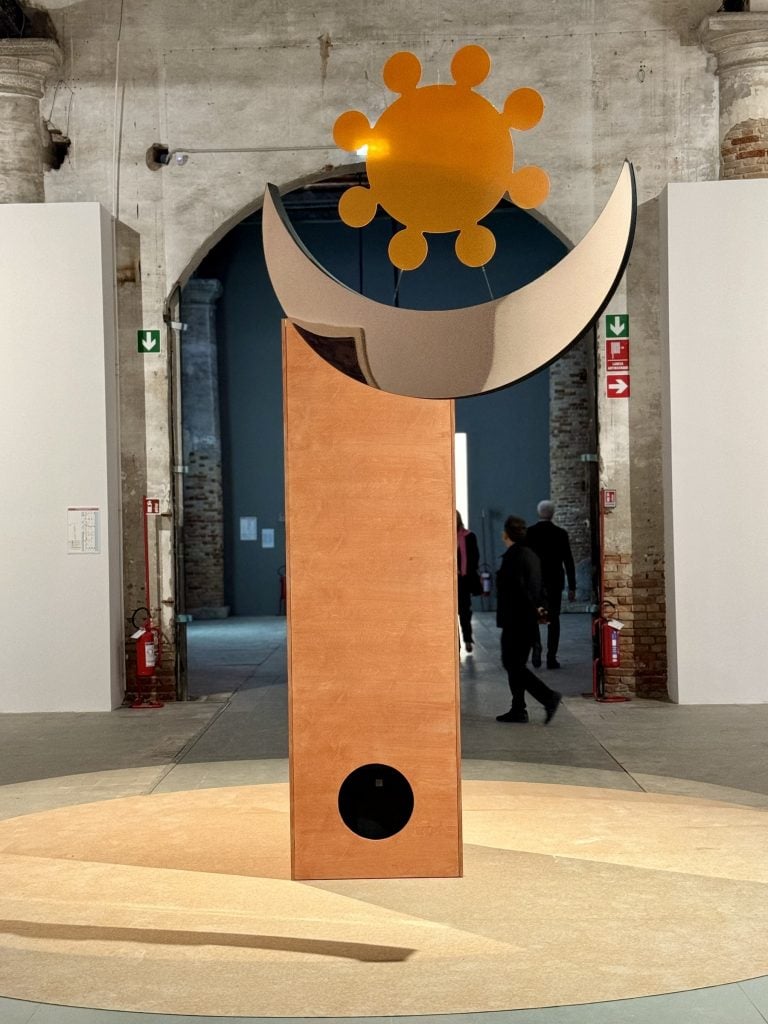 A sculpture of an orange vertical box topped by the shapes of the sun and the moon