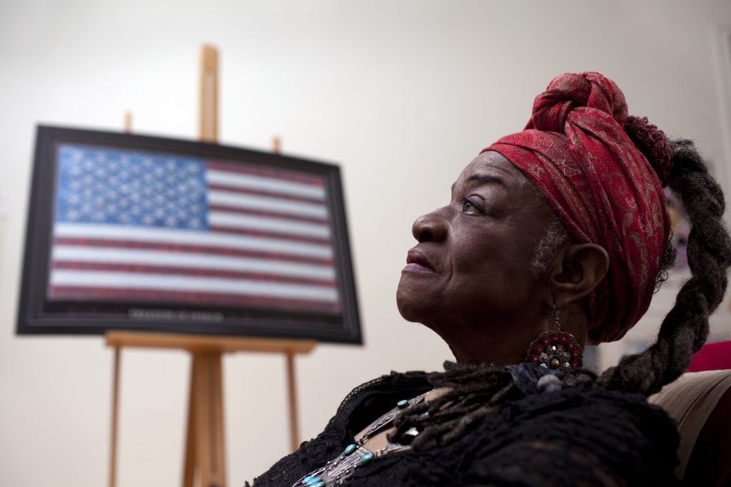 A woman photographed in profile alongside an easel displayed with a painting of an American flag