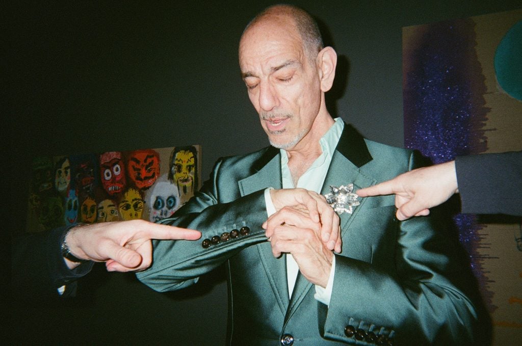 Two fingers pointing at an artist wearing a flashy suit.