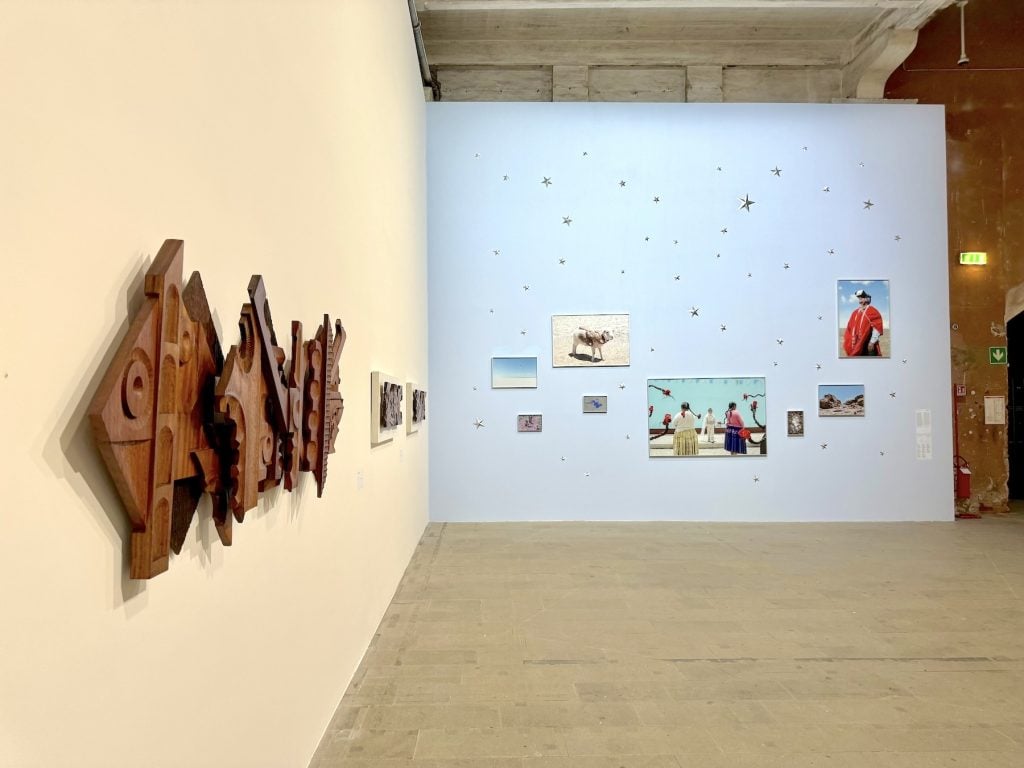 An abstract wood sculptural relief hanging on the wall, and a suite of photographs in the distance