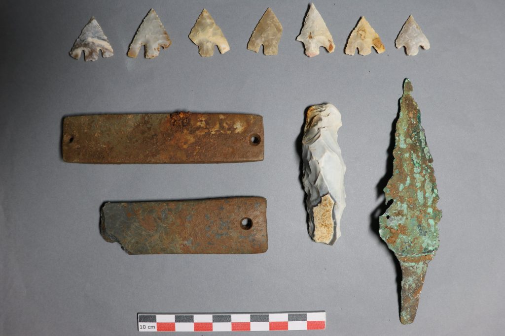 A photograph of Neolithic relics including a row of seven arrowheads and two weathered daggers