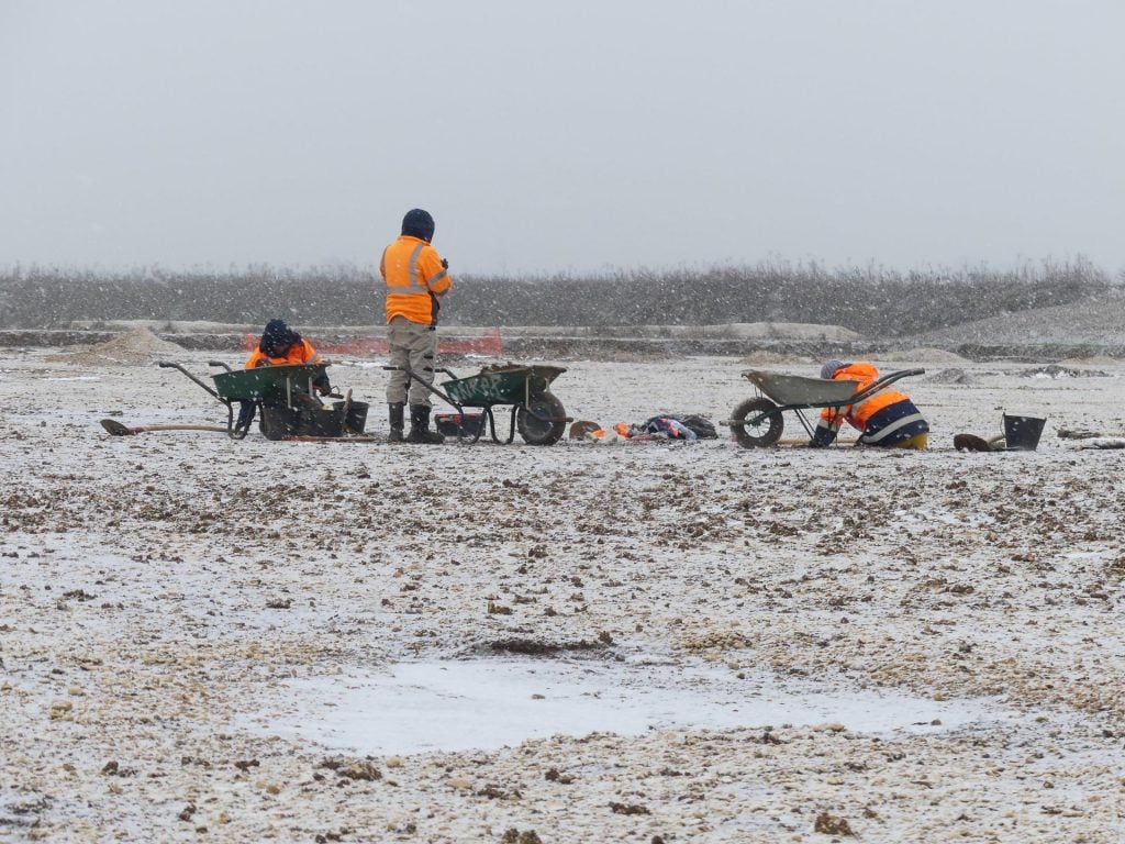 A photograph of crews in orange vests excavating the site on a grey and snowy day