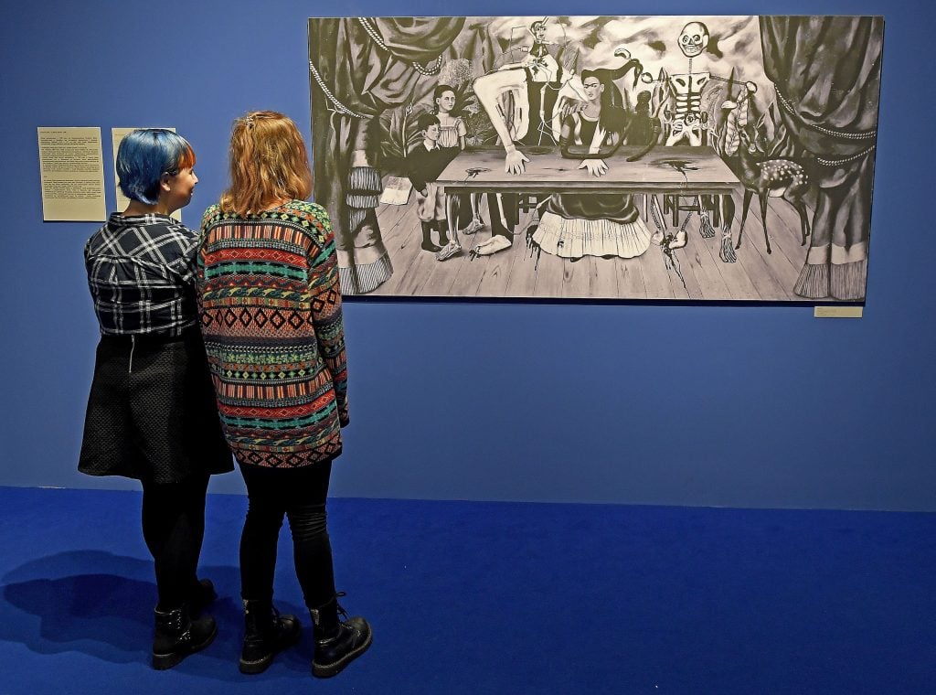Two museum visitors look at a reproduction of Frida Kahlo's painting "The Wounded Table."