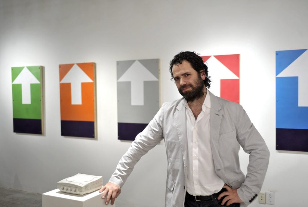 A bearded man stands in an art gallery.