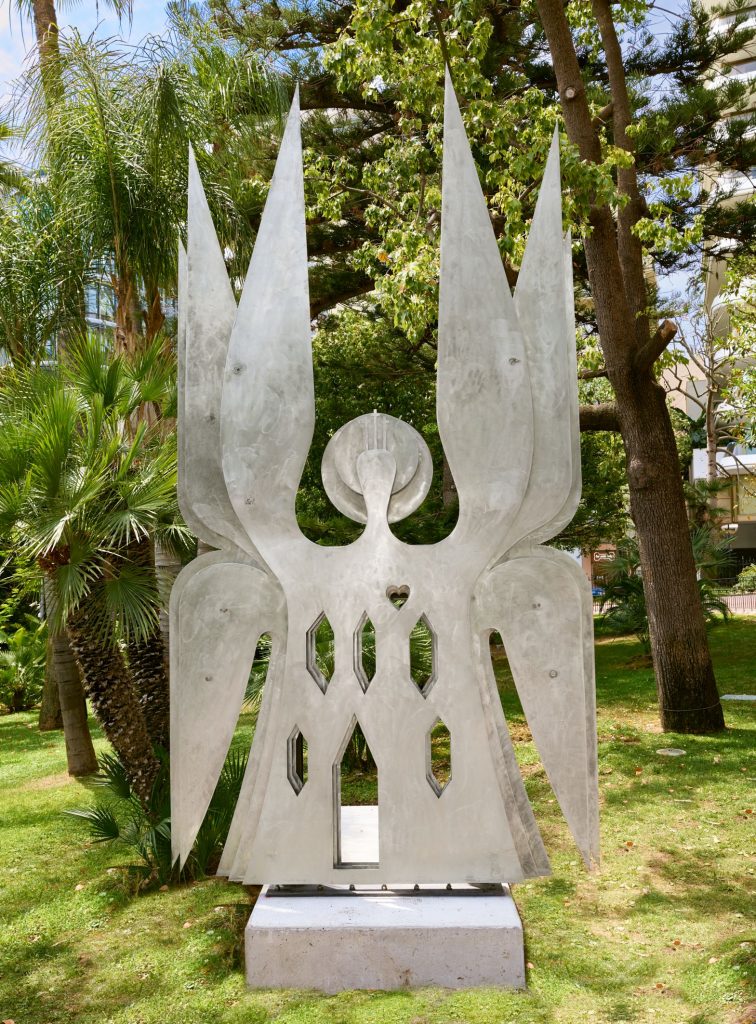 Steel symetrial sculpture installed in a lush green garden.