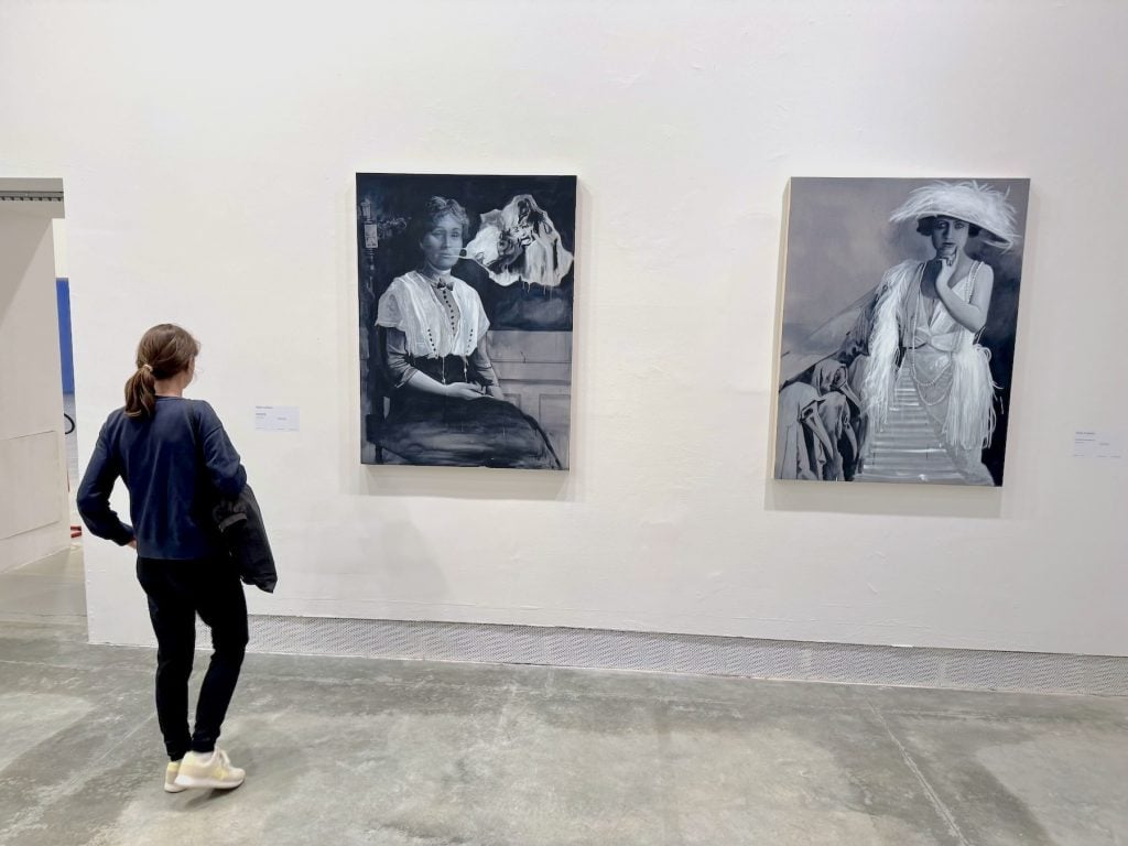 A woman looks at two grayscale figurative paintings of women