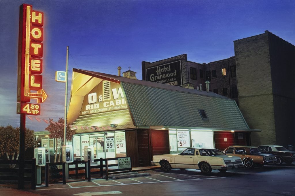 Using photorealism, a painting of a barn-style building with a neon size reading "Hotel" and vintage cars in the parking lot.