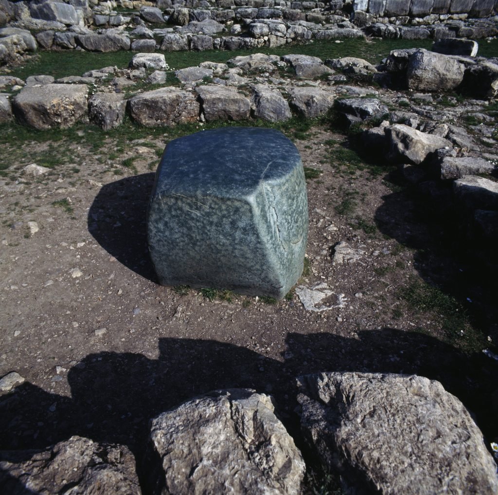 A large green stone surrounded by the remains of an ancient temple in Hattusa, Turkey