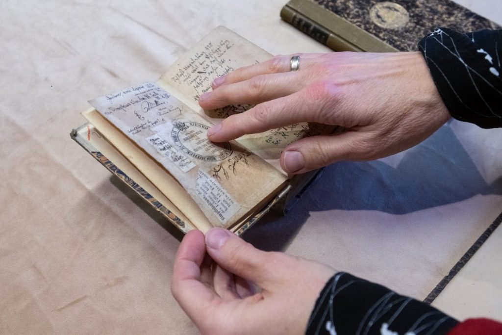 A photo of two hands delicately paging through an old book on a beige background