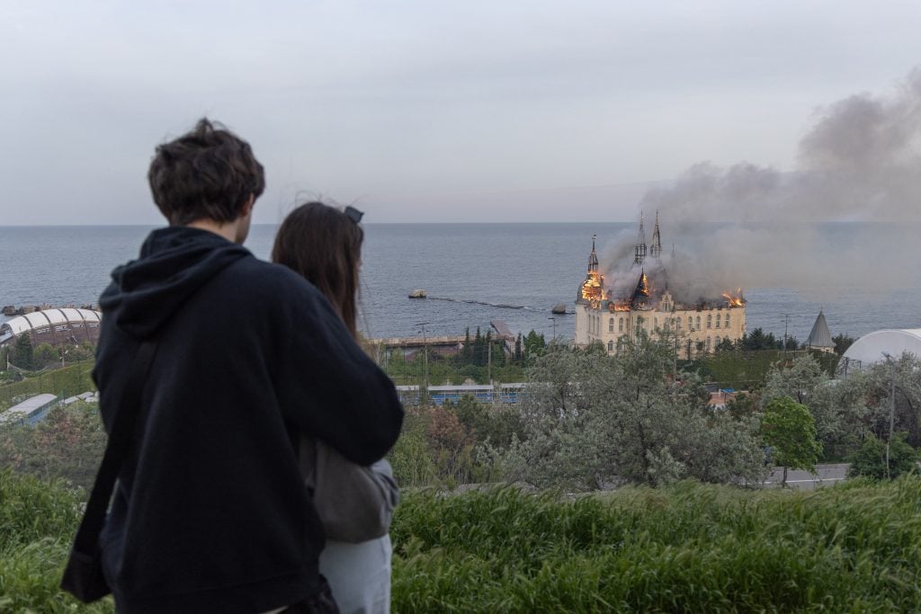Onlookers watch a castle-style building near the shore burn after a missile strike