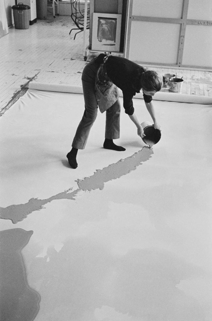 A woman, artist Helen Frankenthaler, pouring paint on a large canvas stretched across the floor