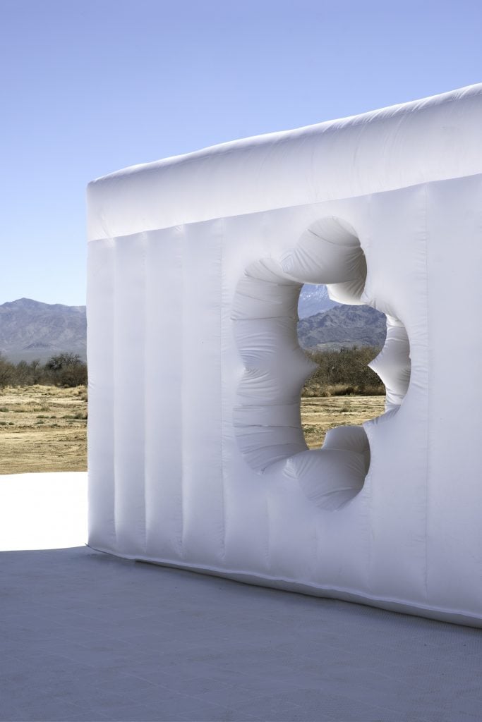 A photograph of the corner of an all-white inflatable building with a flower-shaped cut out amidst a desert background
