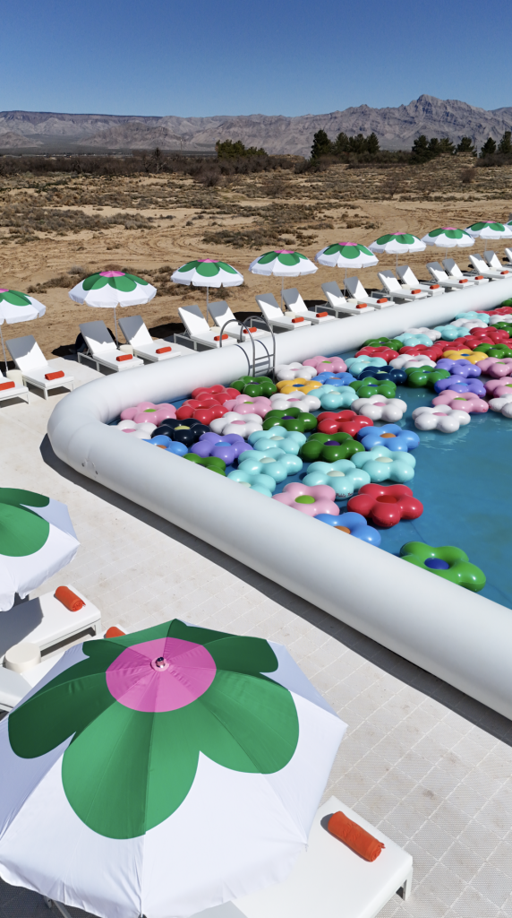 An aerial photograph of the corner of an inflatable white pool with colorful floral toys in the middle of the desert