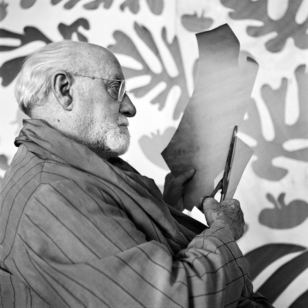 a black and white photo of Matisse cutting a piece of paper with scissors