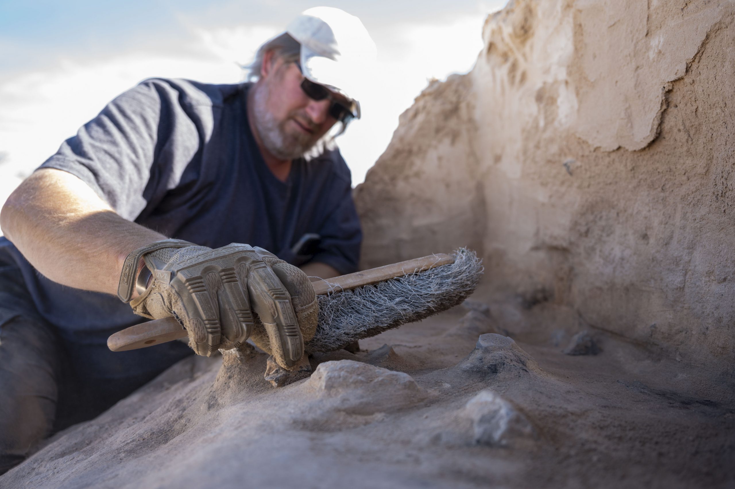 A photograph of a man dusting off a desert archaeological site