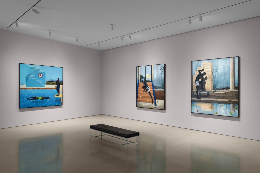 a gallery with thee artworks on view, each painting is dominated by the color blue. 