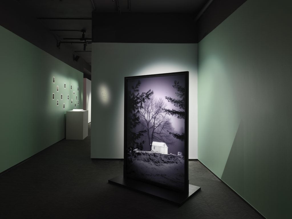 Installation view in a darkened gallery space with illuminated black and white photographs by Daniel Arsham.