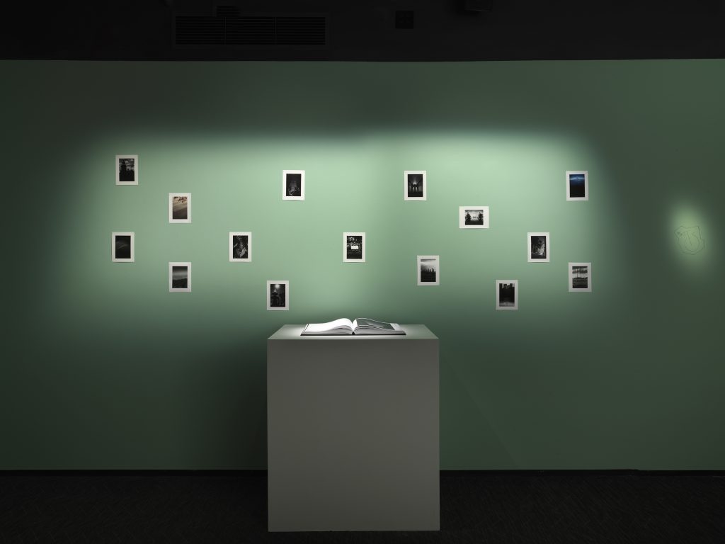 Installation view in a darkened gallery space with illuminated black and white photographs by Daniel Arsham.