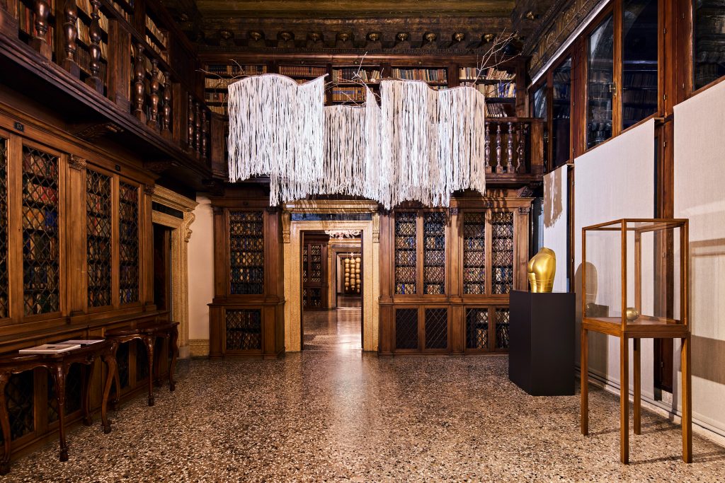 Exhibition in venice in a historic palazzo, a historic wood and book lined library with a hanging sculpture.