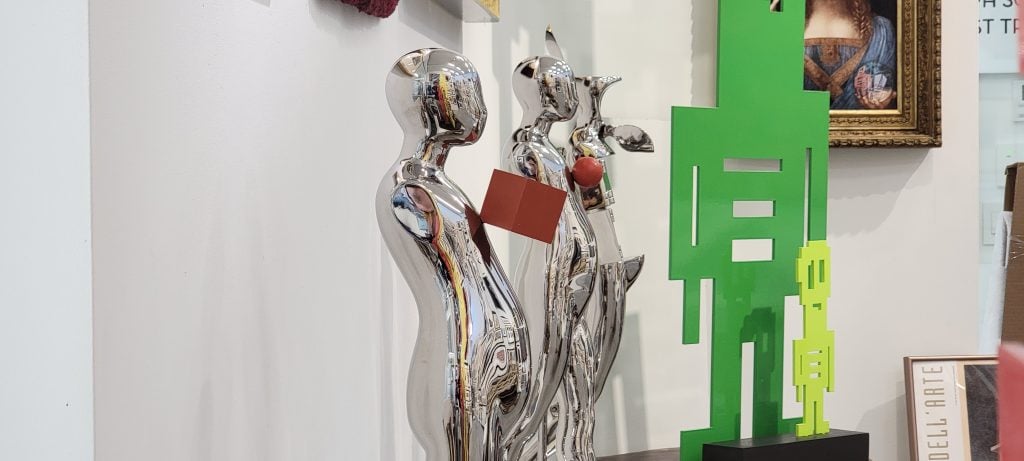 Close up of sculptures, on the left chrome figurines and on the right a flat, kelly green outline of a robot.