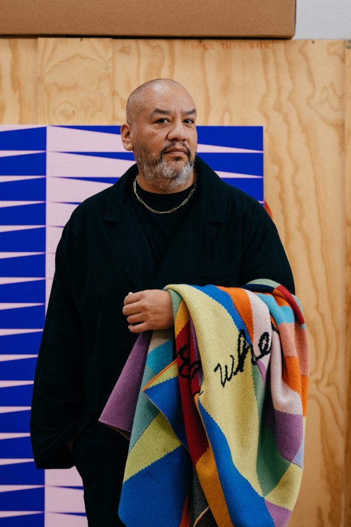 artist jeffrey gibson holding a colorful patchwork blanket